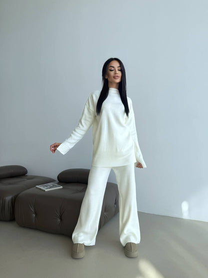 Person wearing a white outfit standing in a minimalistic room with a gray sofa.