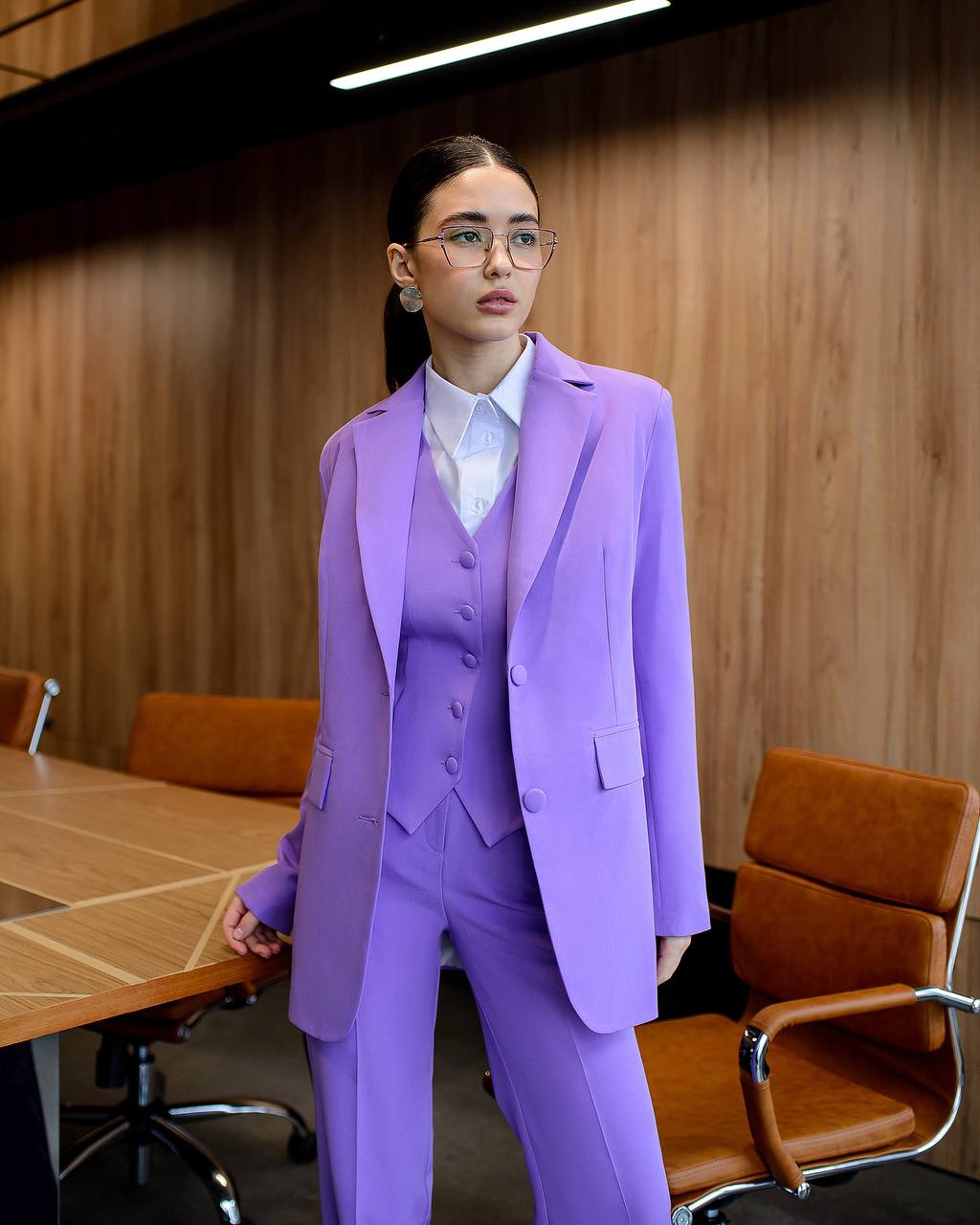 Woman in a purple suit standing in a conference room with wooden walls and furniture.
