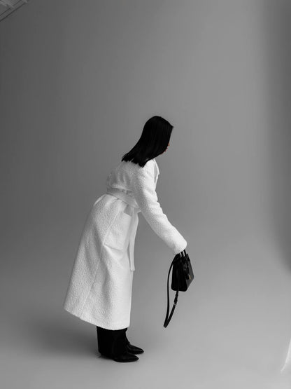 Person wearing a white coat holding a black bag against a plain background