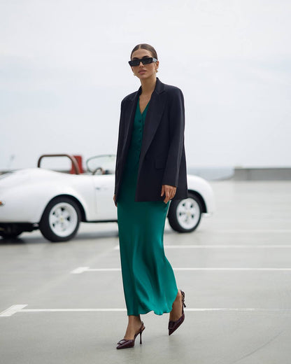 Woman in a green dress and black blazer standing in a parking lot with a white car in the background.