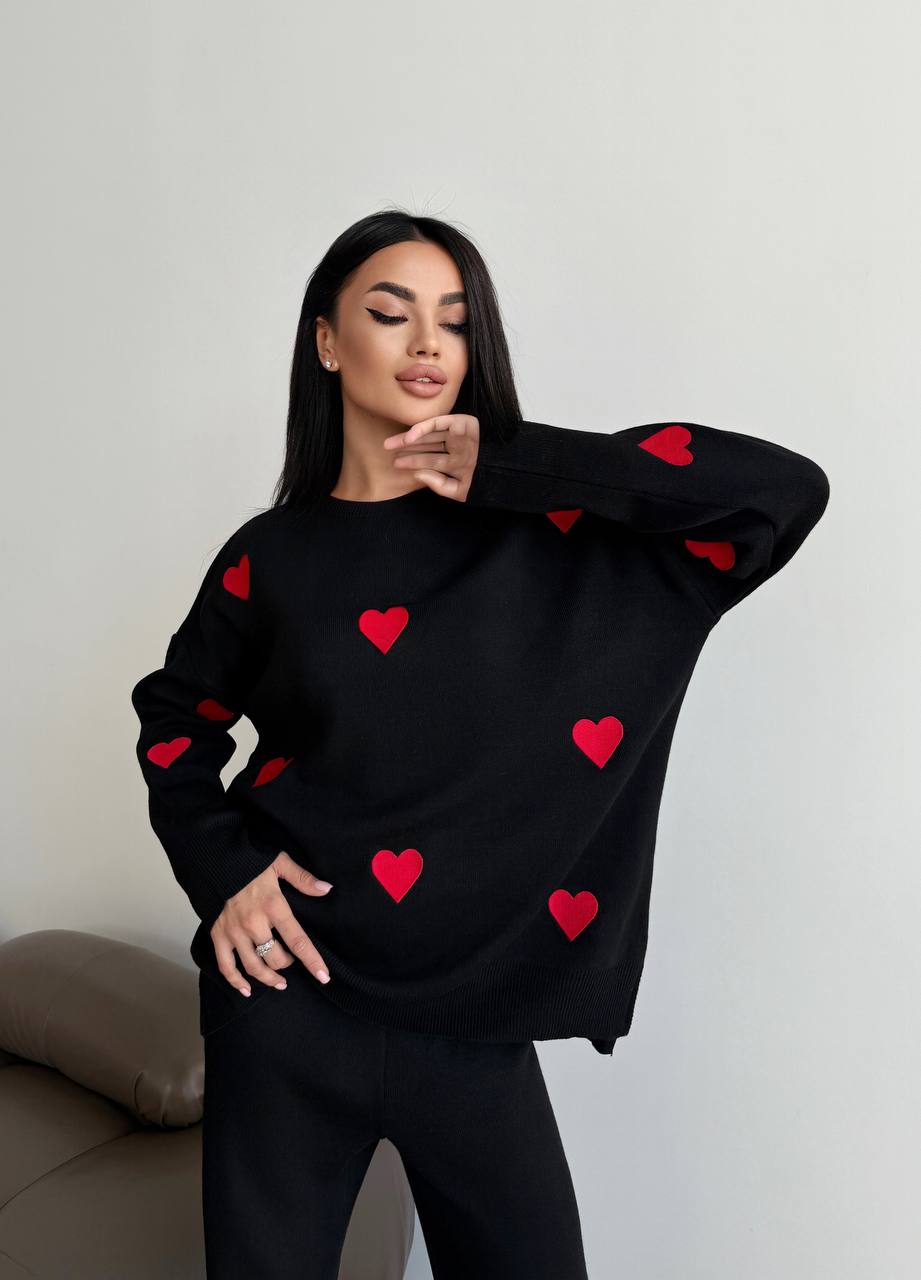 Woman wearing a black sweater with red heart patterns on a plain background