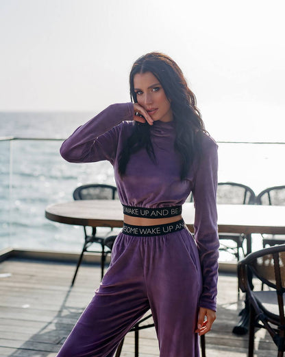 Woman in a purple outfit standing on a rooftop with tables and chairs in the background.