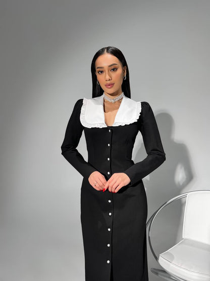 Woman wearing a black dress with white collar against a gray background
