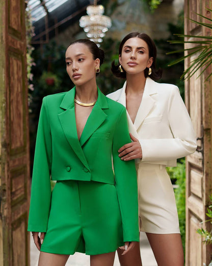 Two women in stylish outfits standing in an elegant indoor setting.