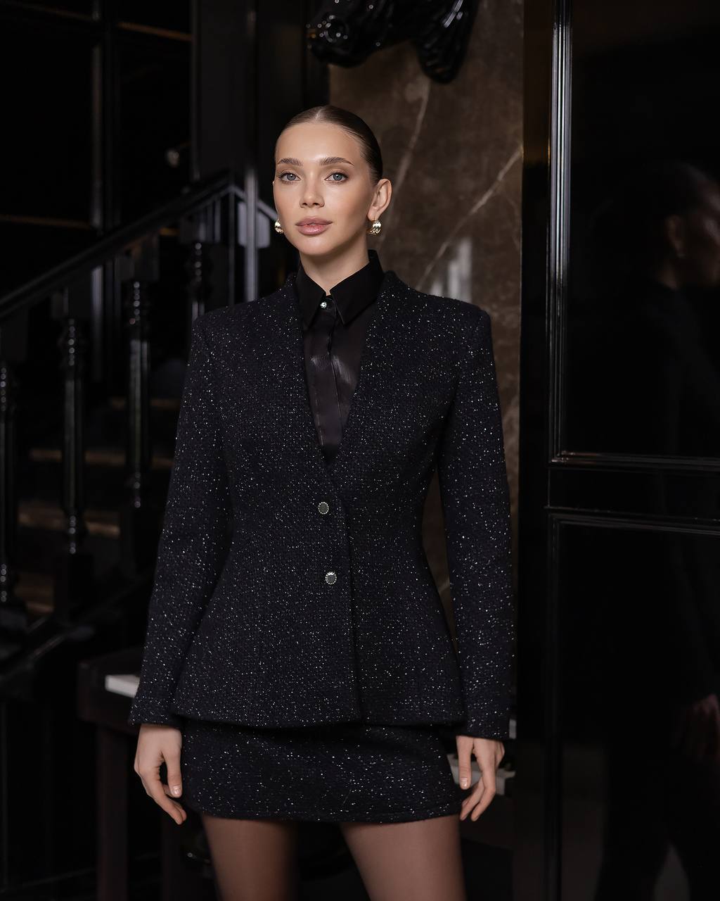 Woman wearing a black textured suit in a dimly lit setting
