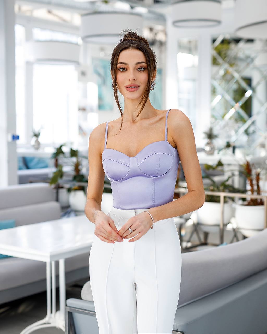 Woman wearing a light purple top and white pants in an indoor setting