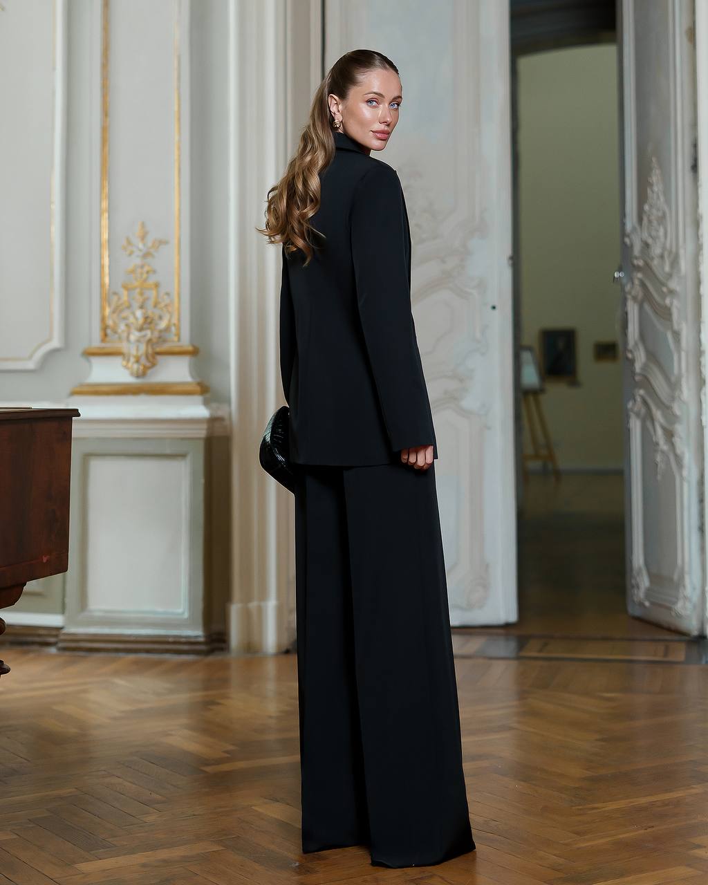 Woman in a black outfit standing in an elegant room with classical decor.