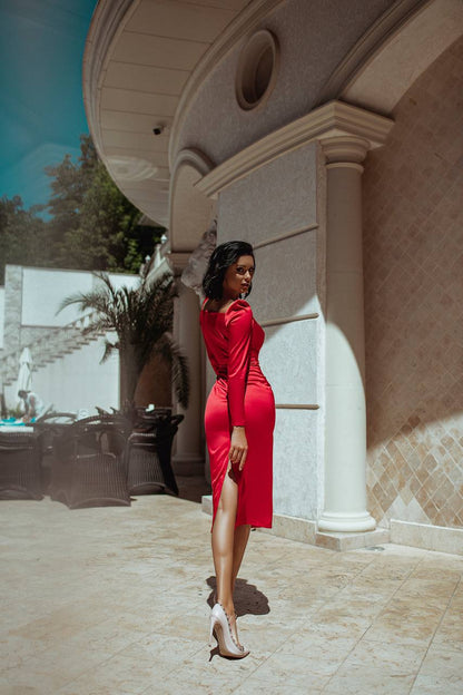 Woman in a red dress standing outdoors near a building with columns.