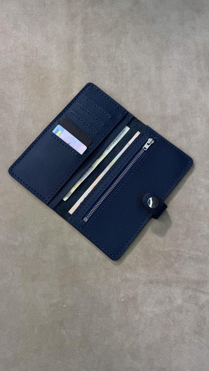 A navy blue leather wallet shown open, displaying its interior features including card slots, a zippered compartment, and a small black snap button closure, placed on a textured gray surface.