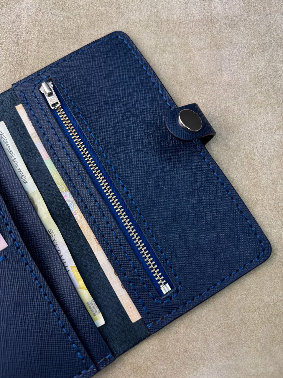 A close-up of a navy blue textured wallet or card holder with a zipper compartment and visible credit cards inside, placed on a beige surface.