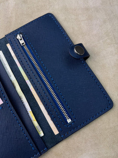 A close-up of a navy blue textured wallet or card holder with a zipper compartment and visible credit cards inside, placed on a beige surface.