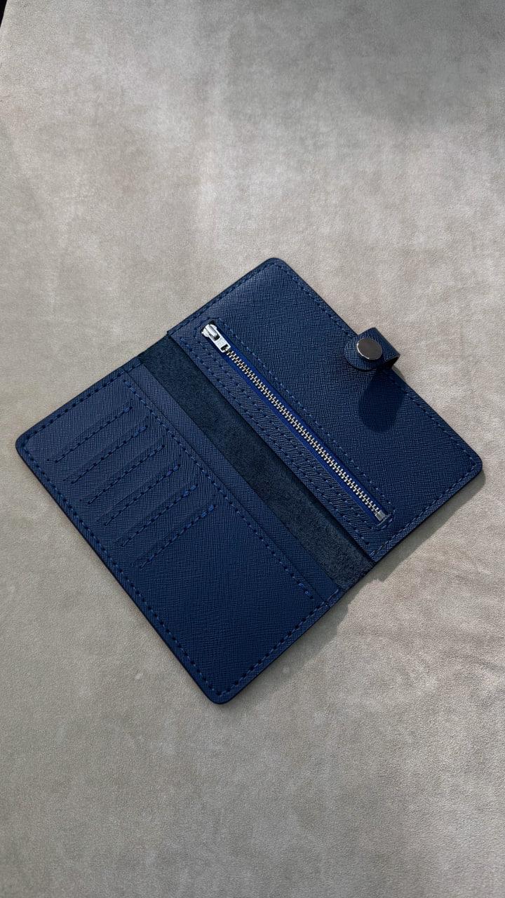 A dark blue leather wallet with multiple card slots, a zippered pocket, and a snap-button closure, shown open on a textured gray surface.