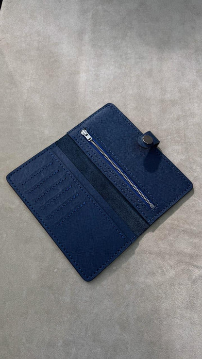 A dark blue leather wallet with multiple card slots, a zippered pocket, and a snap-button closure, shown open on a textured gray surface.