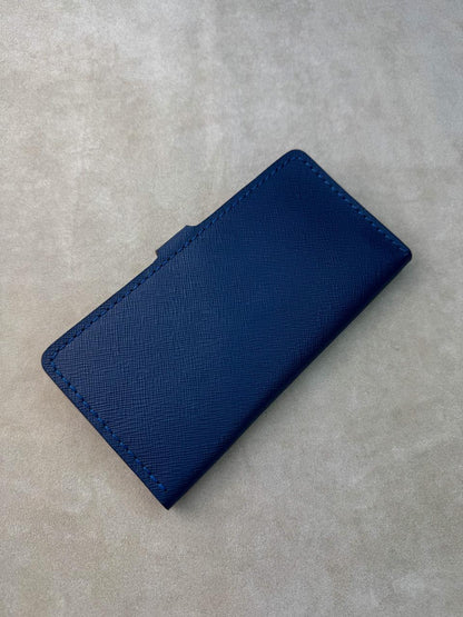 A dark blue textured leather wallet or card holder with matching stitching, shown on a neutral gray textured background.