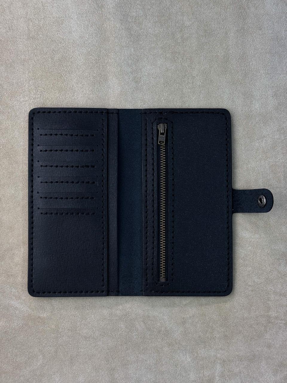 A dark navy blue leather wallet shown open, featuring multiple card slots on the left, a vertical zippered pocket on the right, and a small strap with a metal snap on the far right, laid flat on a textured gray surface.