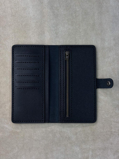 A dark navy blue leather wallet shown open, featuring multiple card slots on the left, a vertical zippered pocket on the right, and a small strap with a metal snap on the far right, laid flat on a textured gray surface.