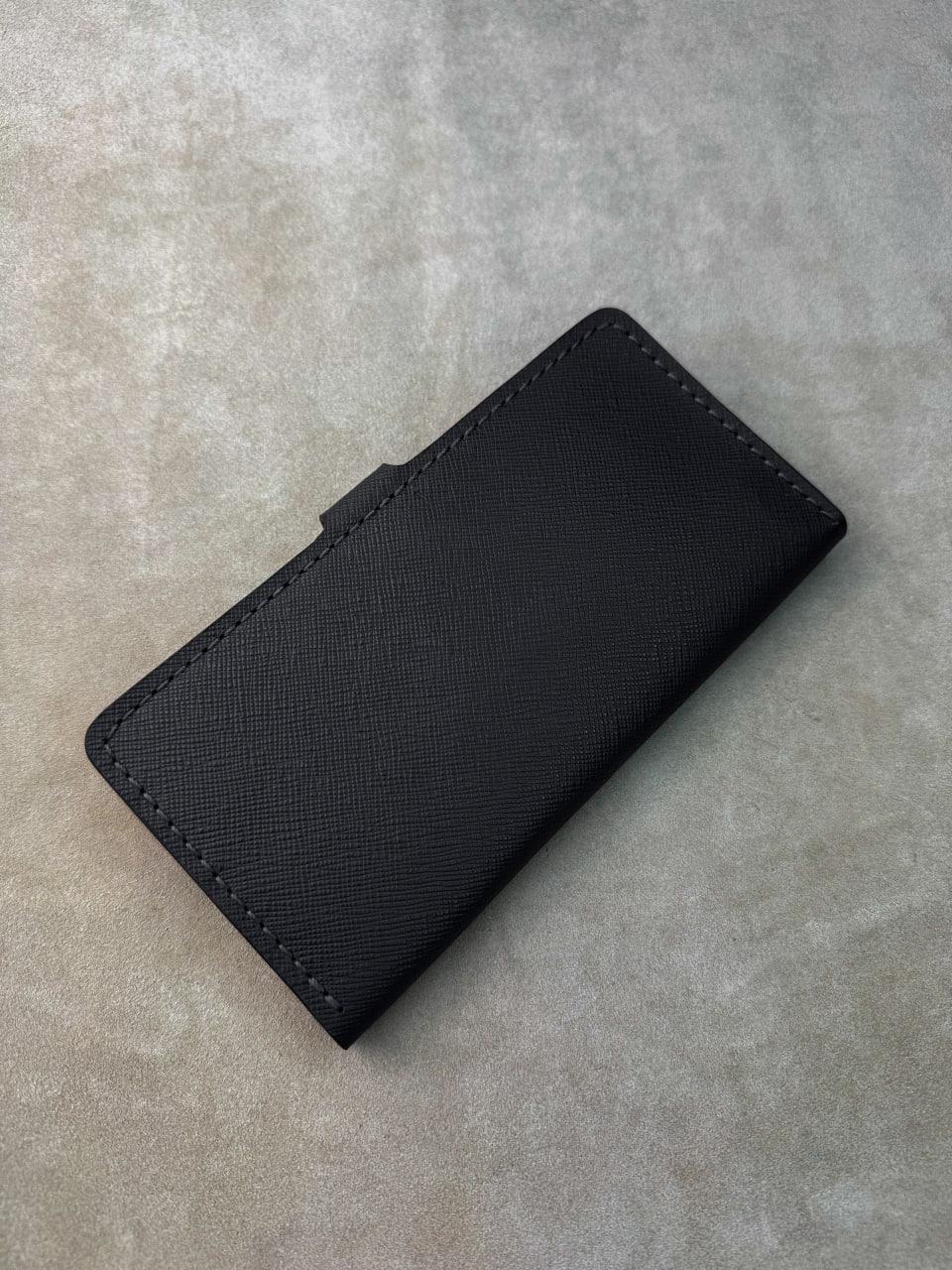 A black textured leather wallet or card holder with visible stitching, photographed on a neutral gray concrete-like surface.
