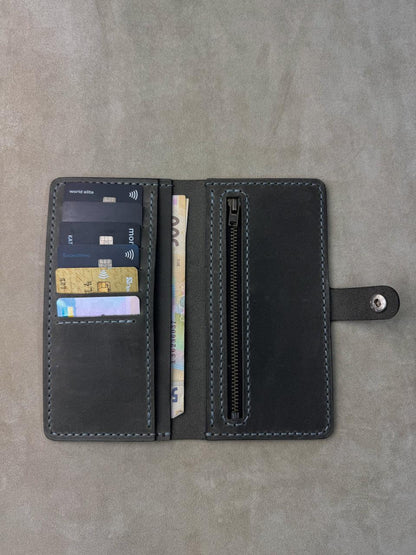 A black leather wallet shown open, displaying its interior features including card slots with credit cards, a zippered compartment, and a strap closure, set against a textured gray background.