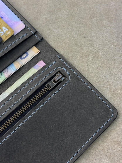 Close-up of a dark gray leather wallet showing card slots with credit cards and a zippered compartment, set against a textured gray background.