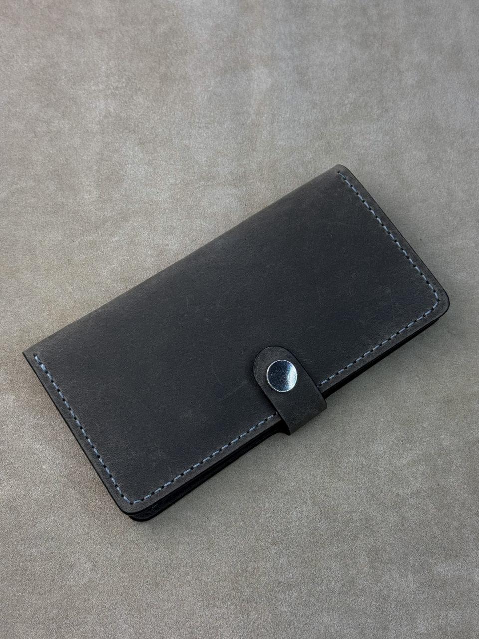 A black leather card holder wallet with a snap-button closure, shown on a textured gray background.