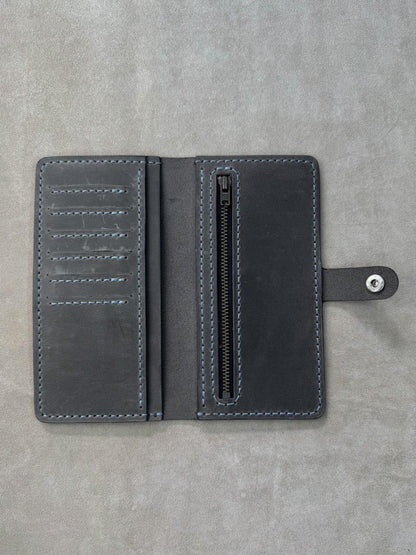 A dark gray leather wallet shown open, featuring multiple card slots on the left, a vertical zippered compartment in the center, and a strap with a silver snap button on the right, set against a textured gray background.