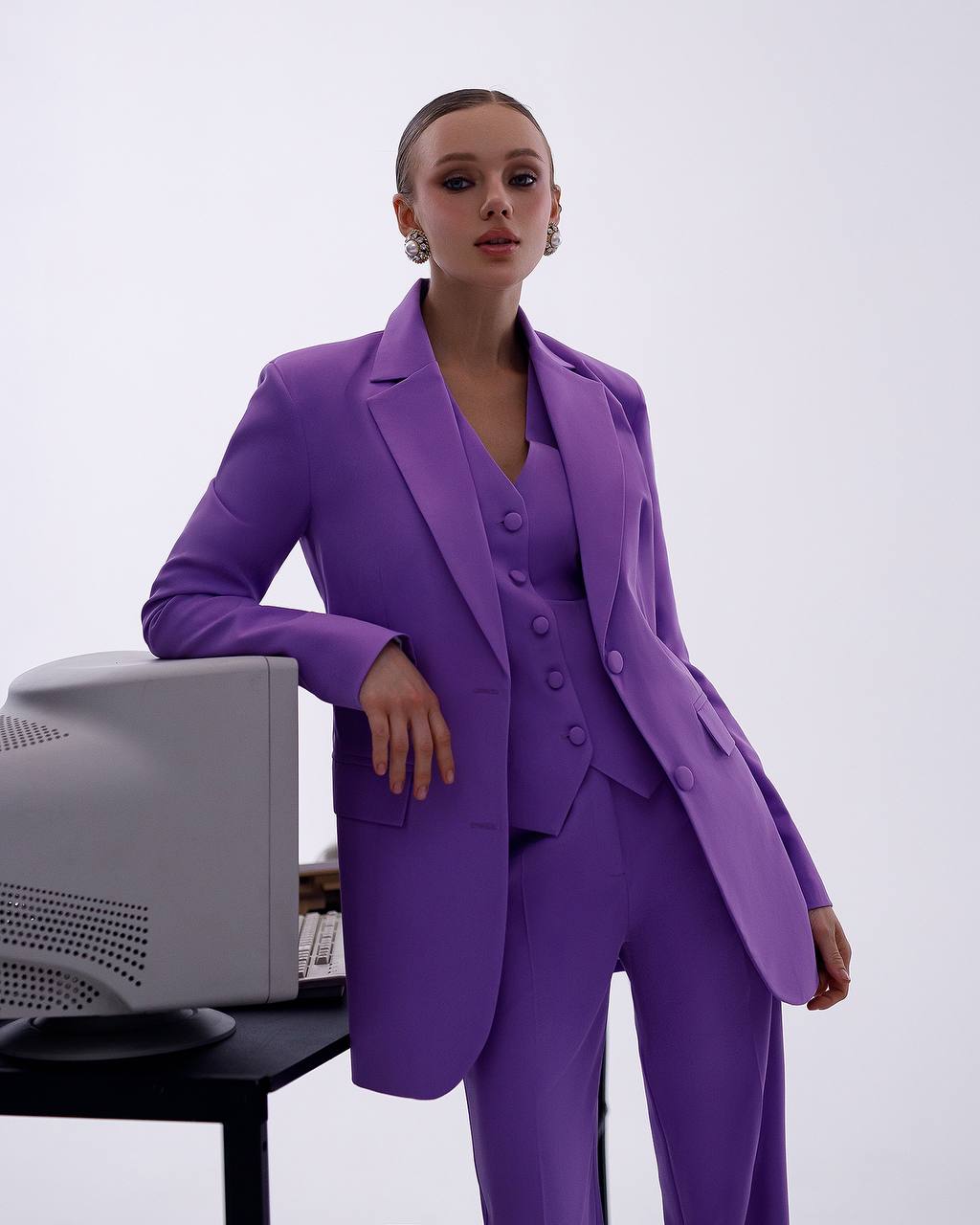 Woman in a purple suit standing next to a computer on a white background