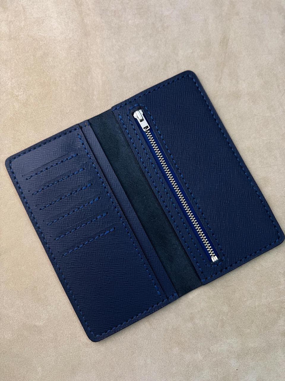 A navy blue leather card holder wallet shown open, featuring a textured leather exterior, a central dark velvet stripe, multiple card slots on one side, and a zippered compartment on the other, photographed on a neutral beige surface.