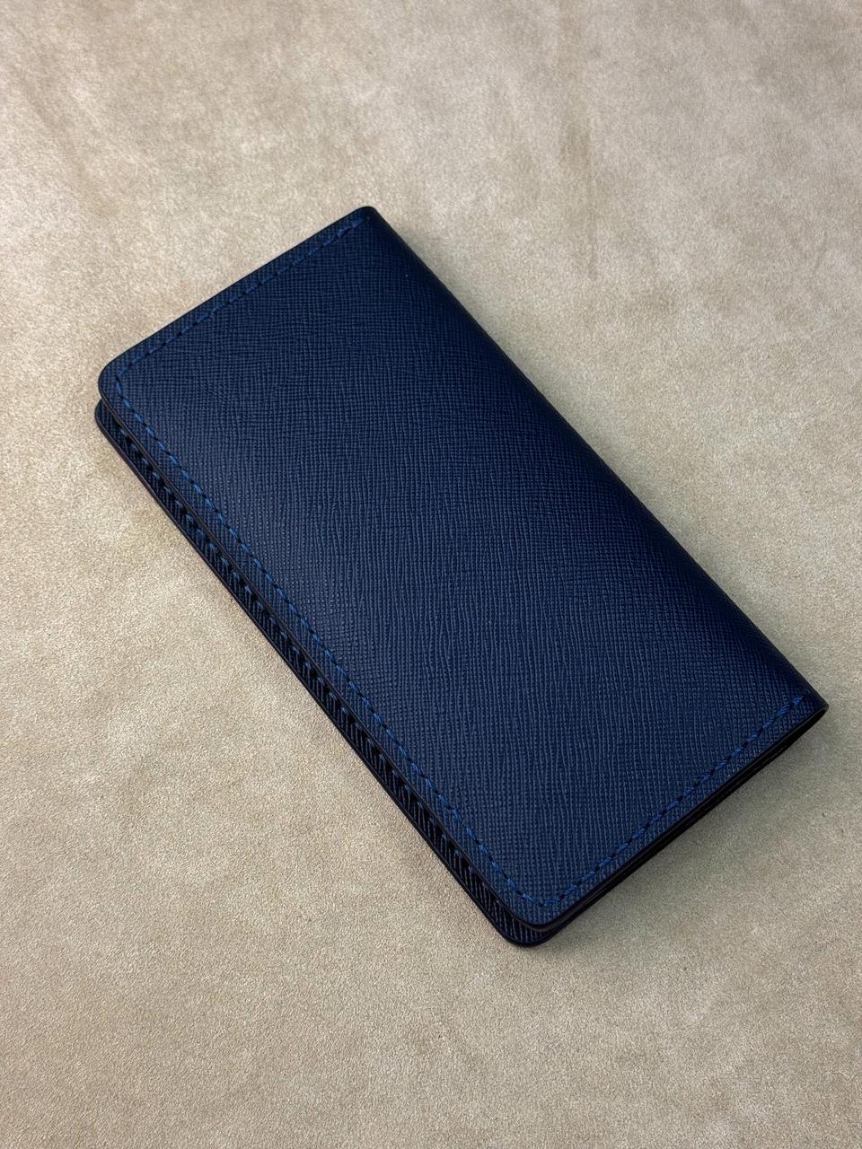A dark navy blue textured leather wallet with visible contrast stitching, photographed on a neutral beige textured background.