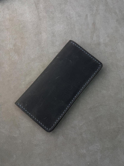 A black leather card holder or wallet with visible contrast stitching, photographed on a textured gray surface.