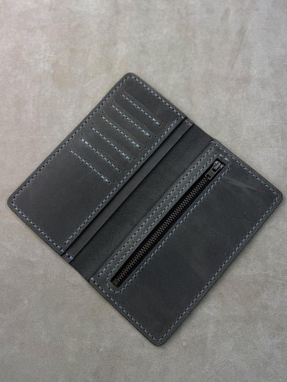 A dark gray leather wallet shown open, displaying its interior compartments, including card slots, a zipper pocket, and contrast stitching, set against a textured gray background.