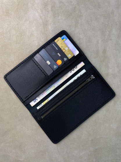 A black leather wallet shown open, displaying its interior compartments filled with sample credit cards and a banknote, placed on a textured beige surface.