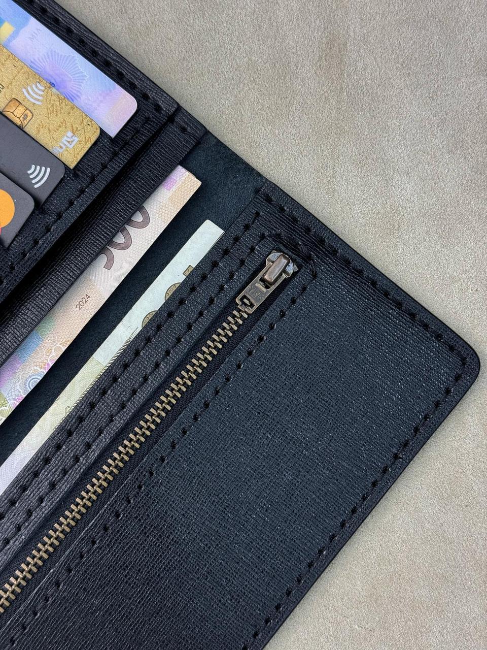 A close-up of an open black textured wallet showing card slots, cash compartments, and a zippered pocket, photographed on a neutral beige surface.