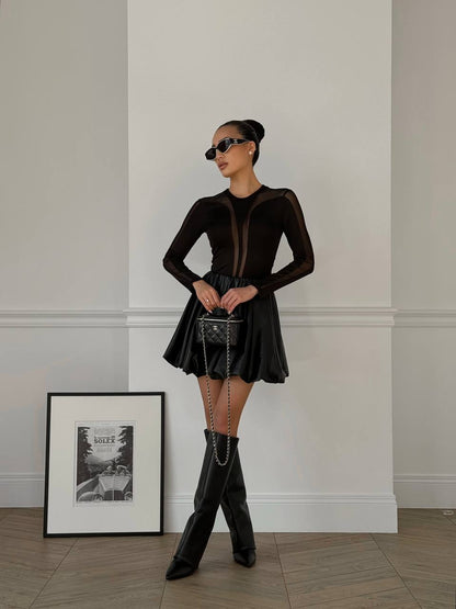 Woman in a black outfit with knee-high boots standing in a room with a framed picture on the wall.