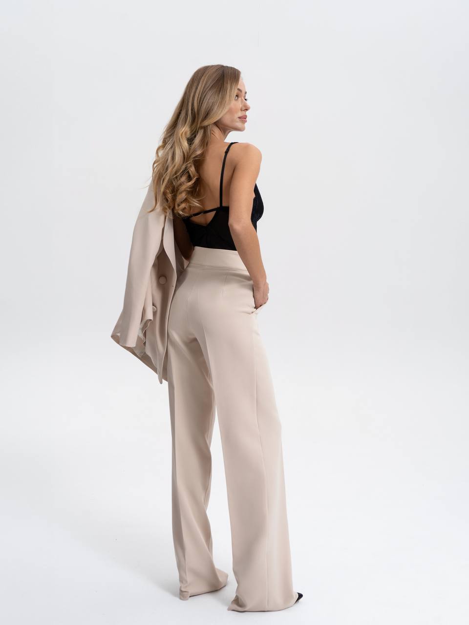 Woman wearing a black top and beige pants with a beige shawl on a white background