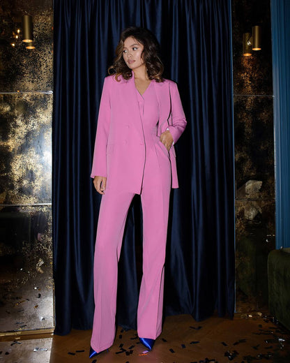 Woman in a pink suit standing against a dark curtain.