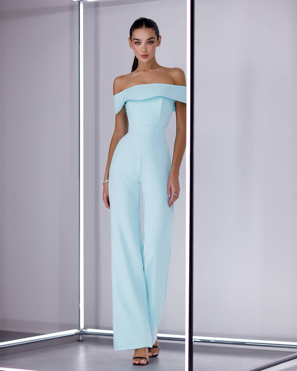 Woman wearing a light blue off-shoulder jumpsuit in a minimalistic setting