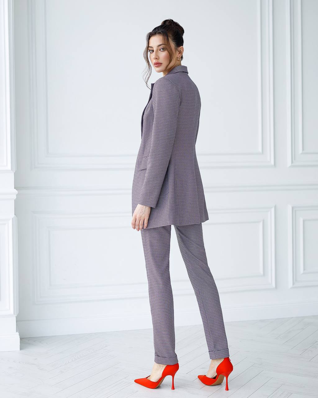 Woman wearing a gray checkered suit with red shoes in a white room.