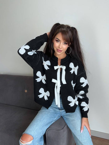 Woman wearing a black cardigan with white floral patterns sitting on a couch.