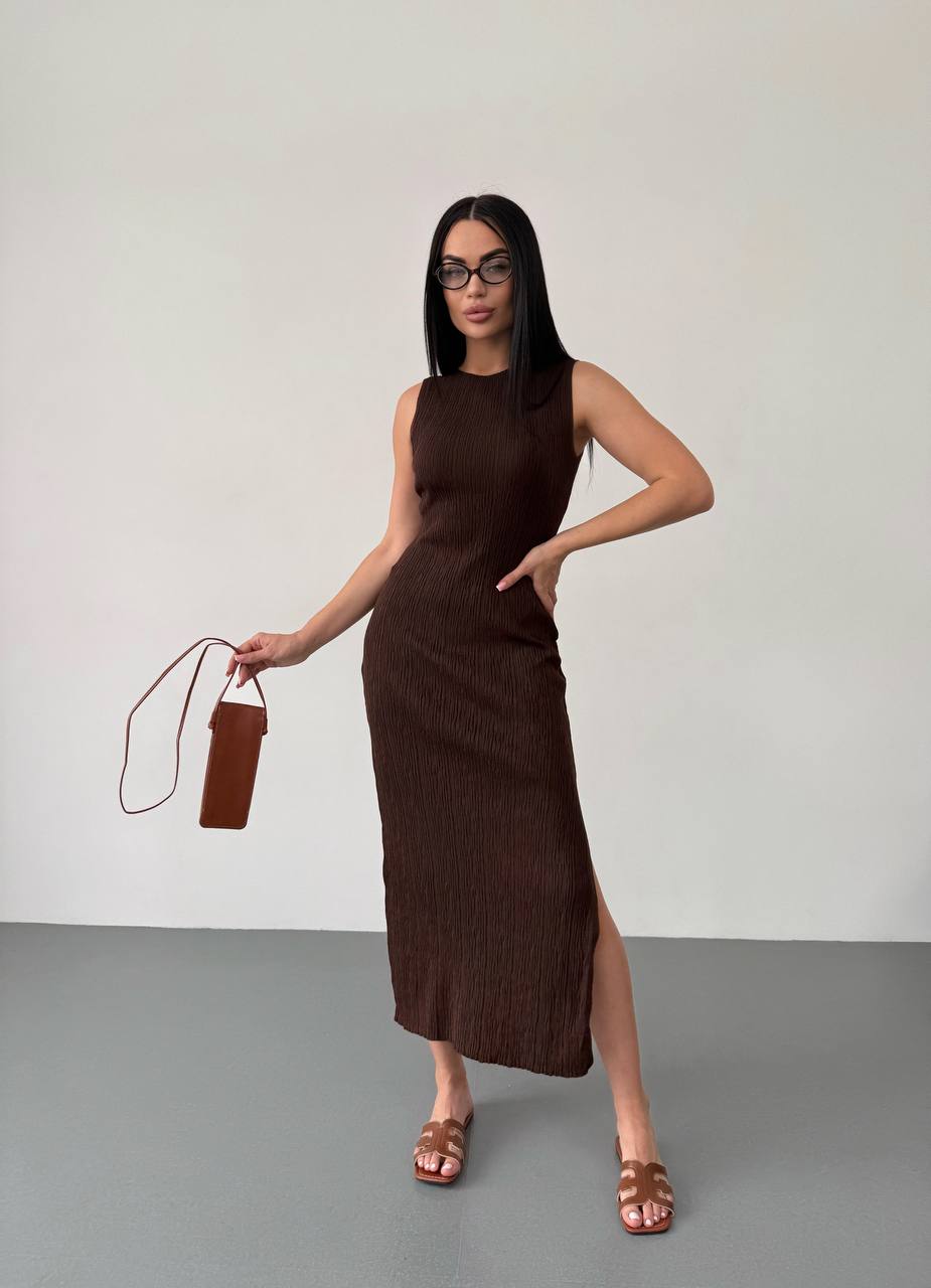 Woman wearing a brown dress holding a matching handbag against a plain background