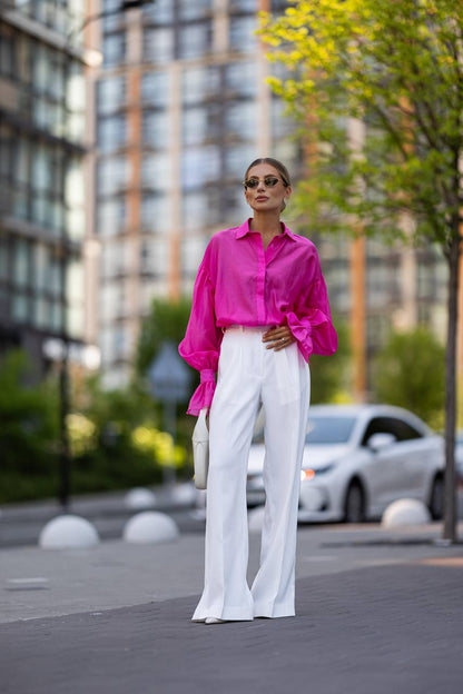 Woman wearing a bright pink shirt and white pants on a city street.