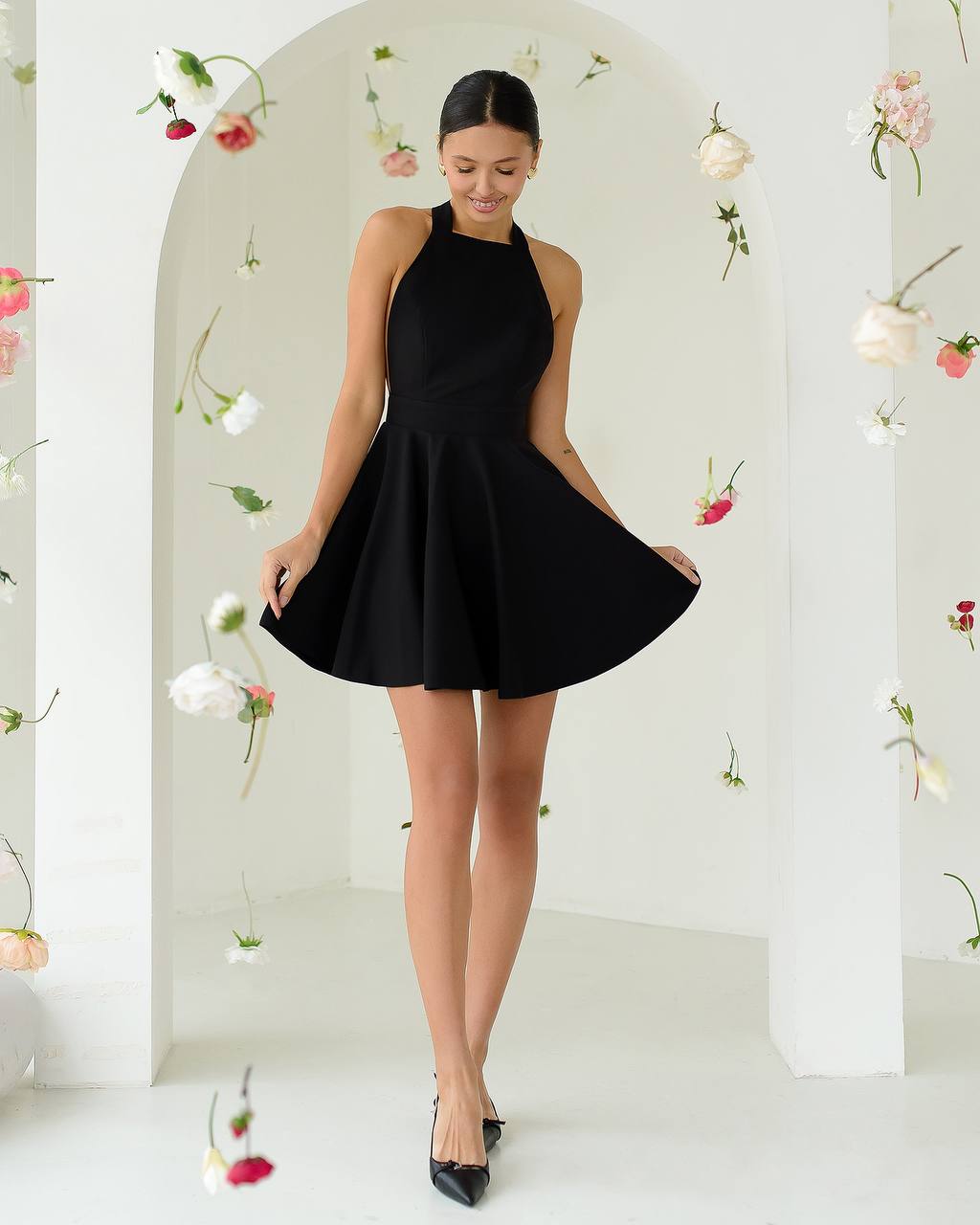 Woman wearing a black dress standing in a decorated room with flowers.