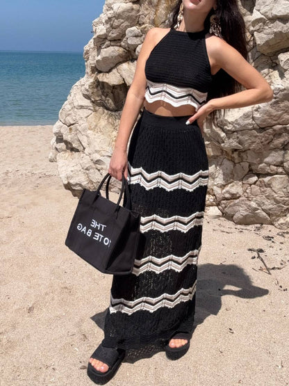 Woman in black and white striped outfit holding a black tote bag by a stone wall with ocean view.