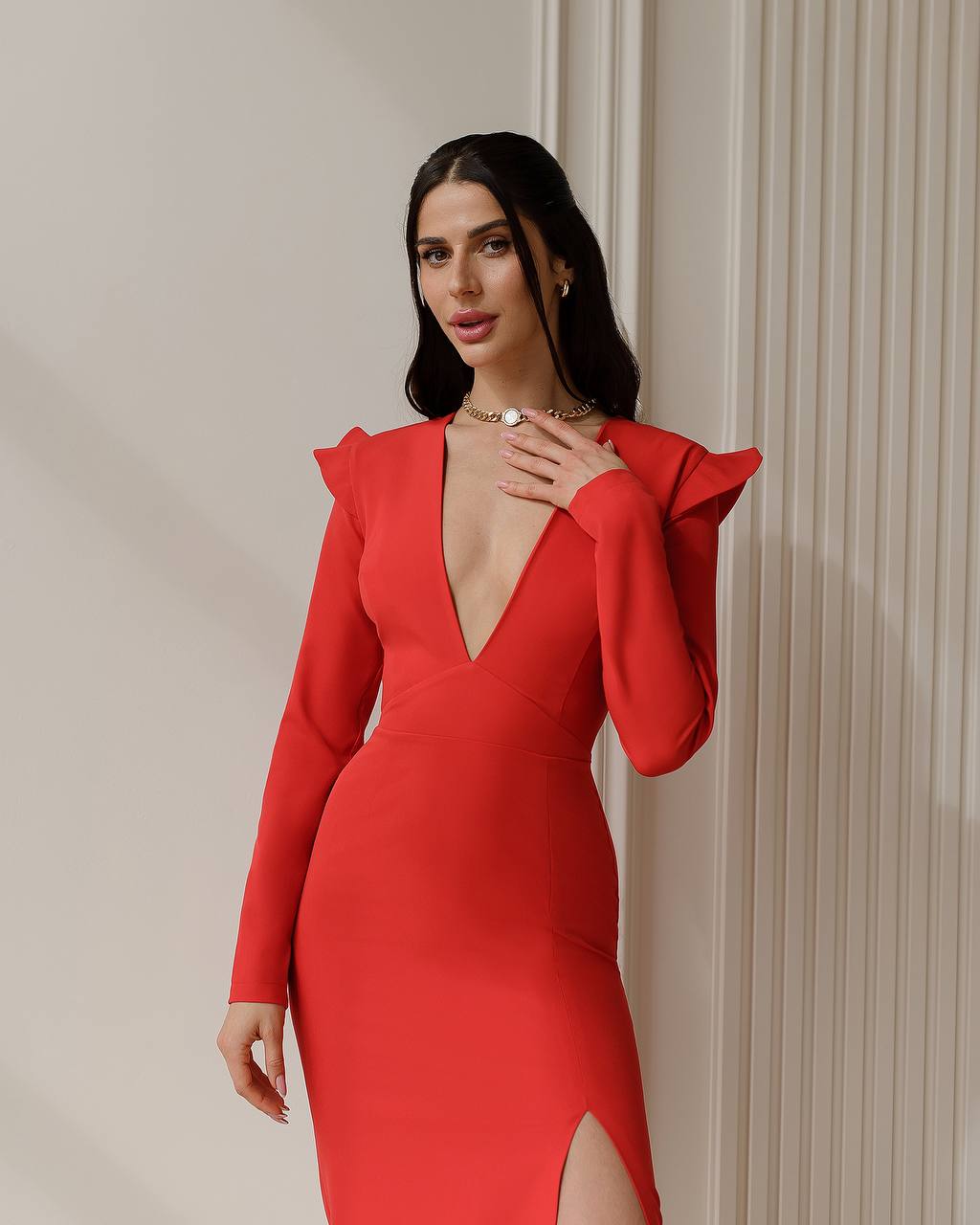 Woman wearing a red dress with a deep neckline and long sleeves against a neutral wall.