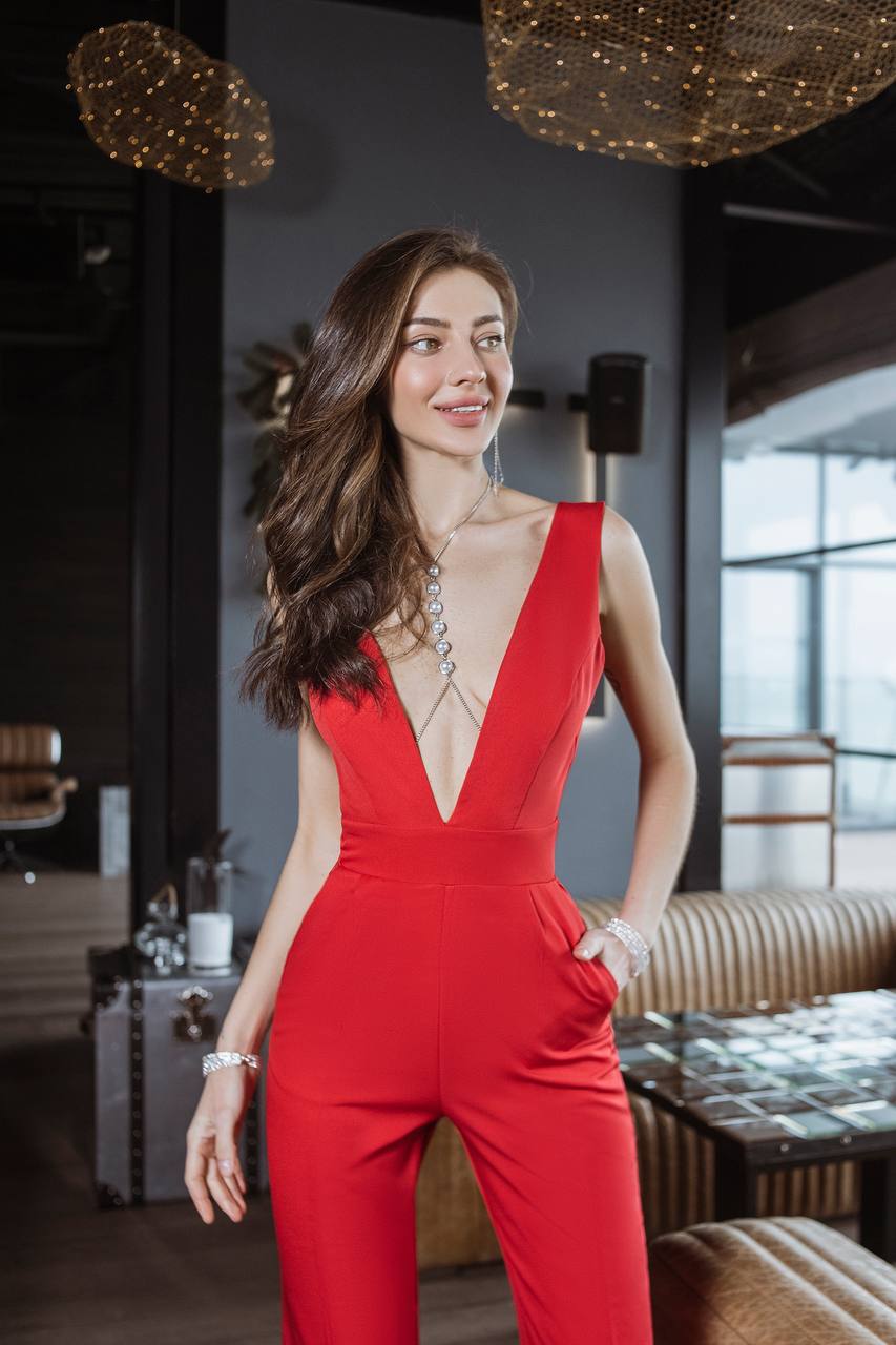 Woman in a red jumpsuit standing in an elegant indoor setting.