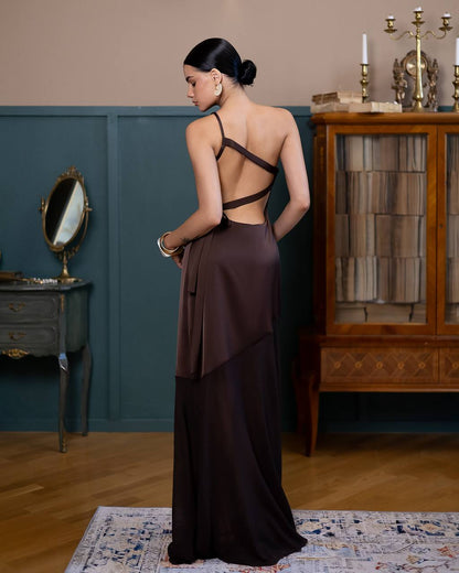 Woman in a long, dark brown dress standing in an elegant room with a mirror and wooden cabinet.