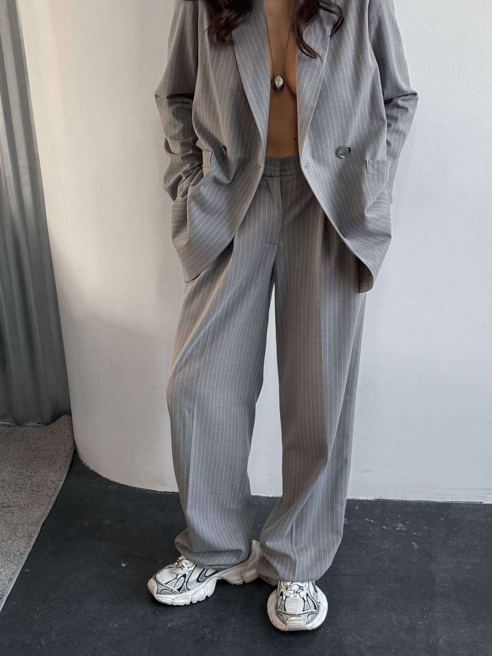 Person wearing a gray pinstripe suit with white sneakers in a minimal indoor setting