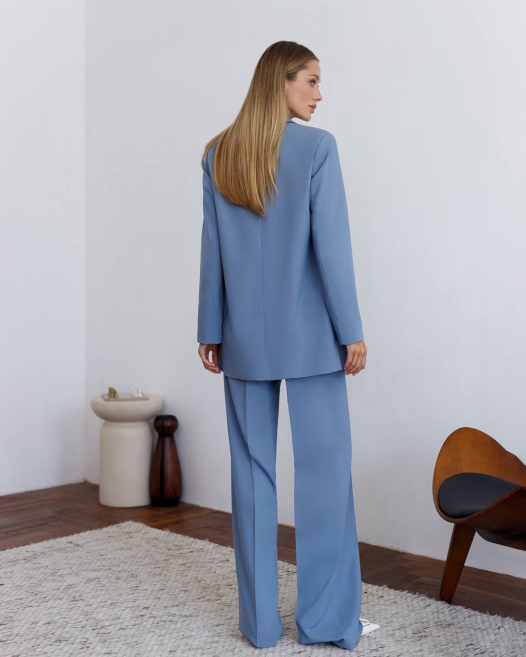 Woman wearing a blue suit standing in a room with a white wall and wooden floor.