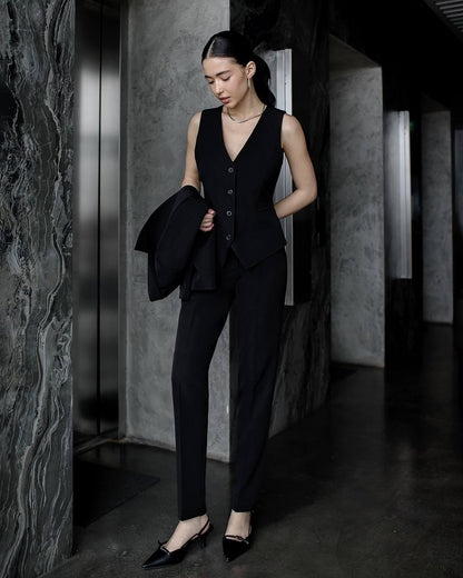 Woman in a black suit standing in a dimly lit room with marble walls.