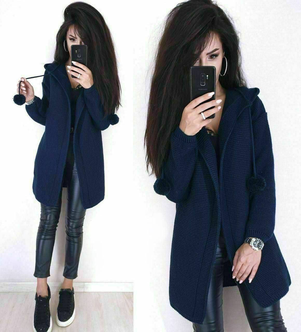 Woman wearing a navy blue coat with pom-pom details, holding a phone.