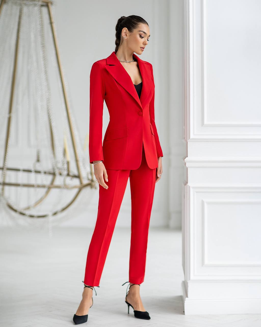 Woman wearing a red suit standing in a minimalistic room with white walls.
